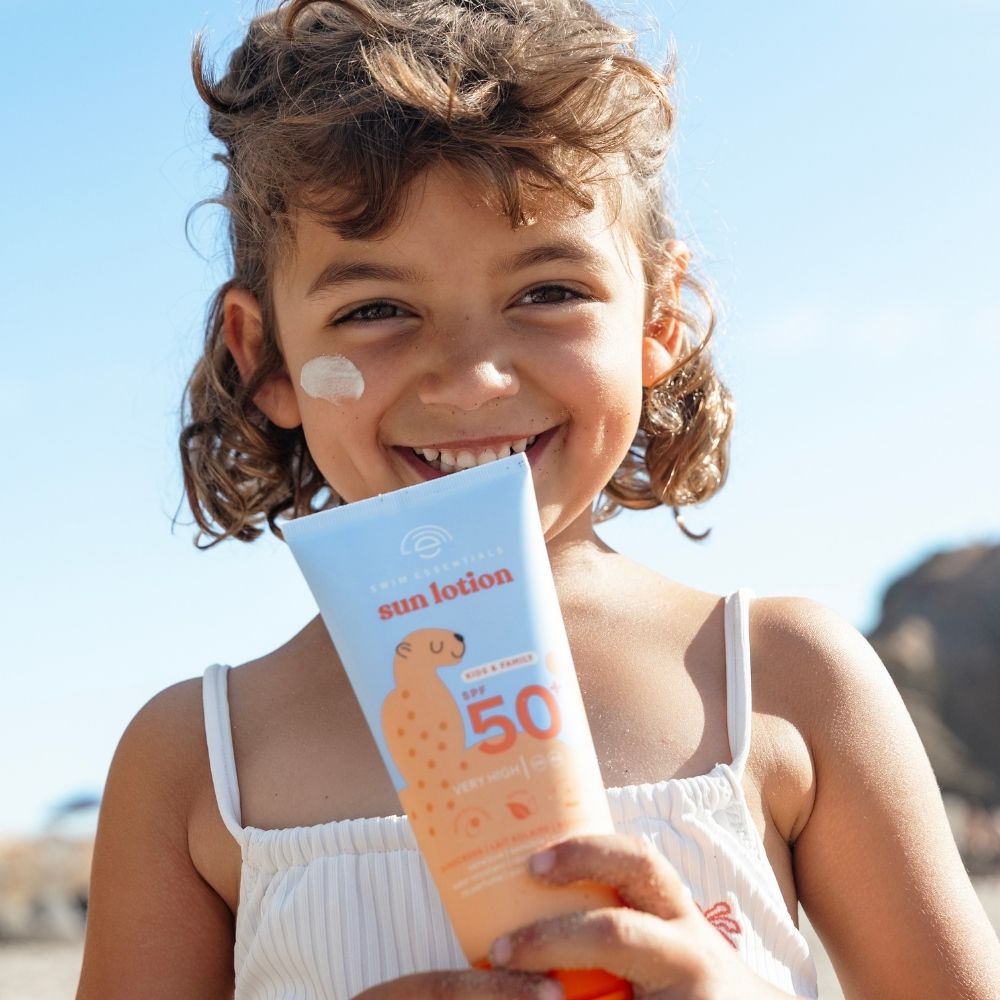 Kislány kezében Swim Essentials SPF 50+ családi naptej érzékeny bőrre, 150 ml-es gazdaságos tubusban.