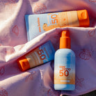 Swim Essentials napvédő termékek: spray és tubusos naptejek egy tengerparti törölközőn.