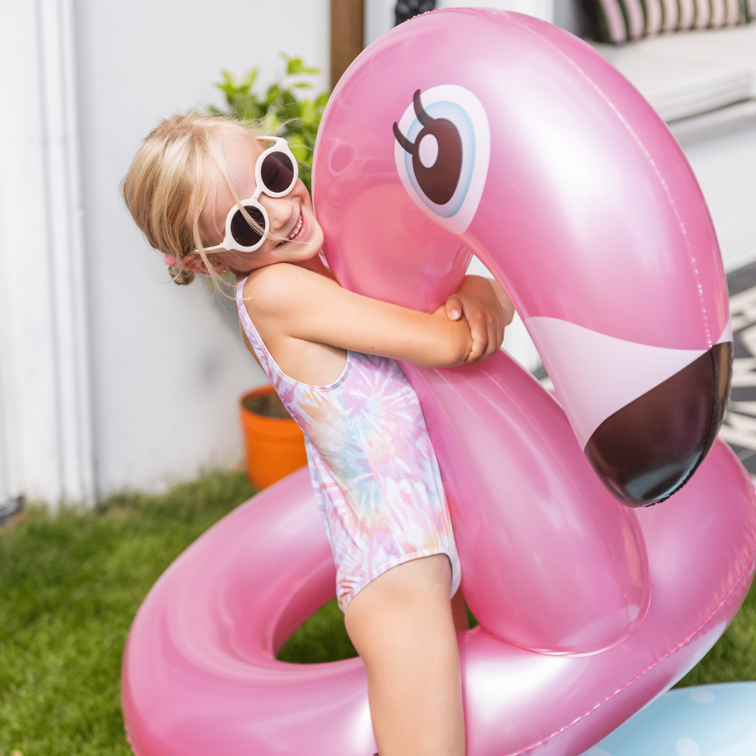 Kislány öleli a Swim Essentials 95 cm-es, rose gold fényű flamingó alakú úszógumiját a kertben.