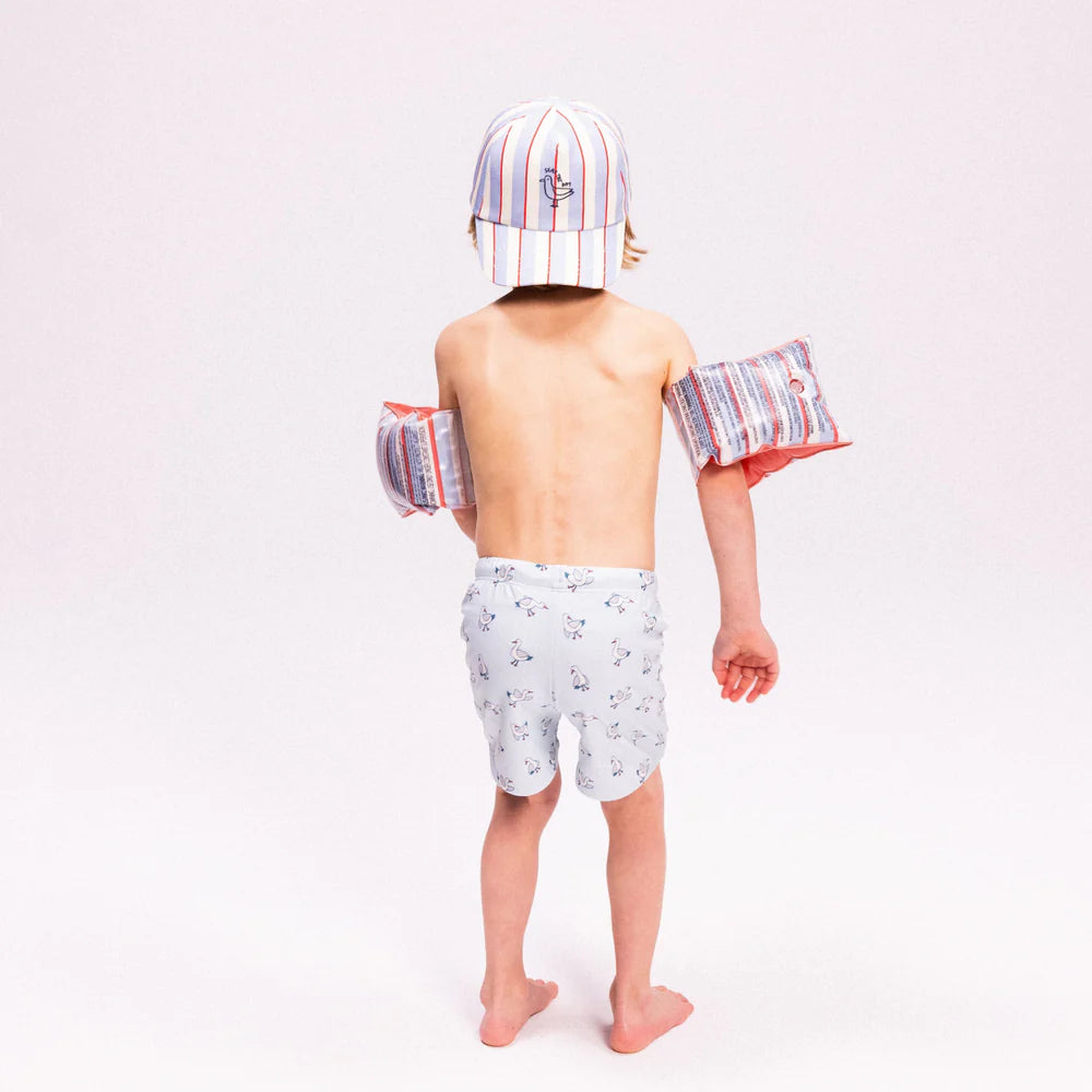 Kisfiú hátulról Swim Essentials „Seas the Day” feliratú, csíkos gyerek baseball sapkában és karúszóval.