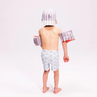 Kisfiú hátulról Swim Essentials „Seas the Day” feliratú, csíkos gyerek baseball sapkában és karúszóval.
