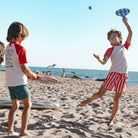 Két gyermek játszik a tengeri csillag mintás Swim Essentials strandtenisz szettel a napfényes tengerparton