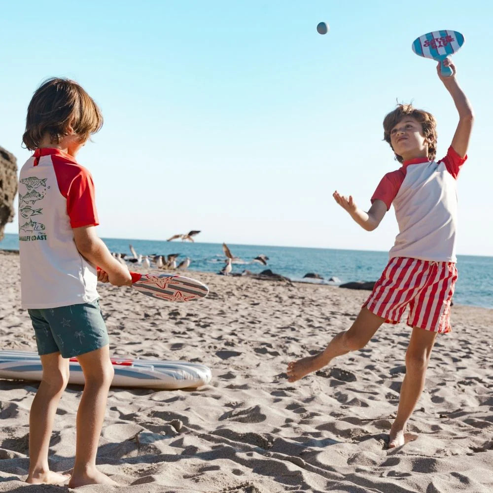 Két gyermek játszik a tengeri csillag mintás Swim Essentials strandtenisz szettel a napfényes tengerparton