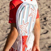 Gyermek hátulról tengeri csillagos fürdőruhában, vállán a Swim Essentials strandtenisz szett átlátszó hordozótáskájával a homokos parton