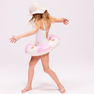 Kislány strandkalapban és fehér fürdőruhában pózol a rózsaszín szívecskés Swim Essentials úszógumival.