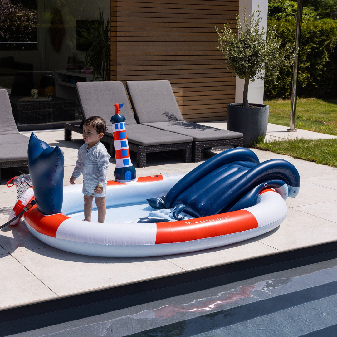 Gyermek pancsol a Swim Essentials tengerész stílusú élménymedencéjében a kertben.