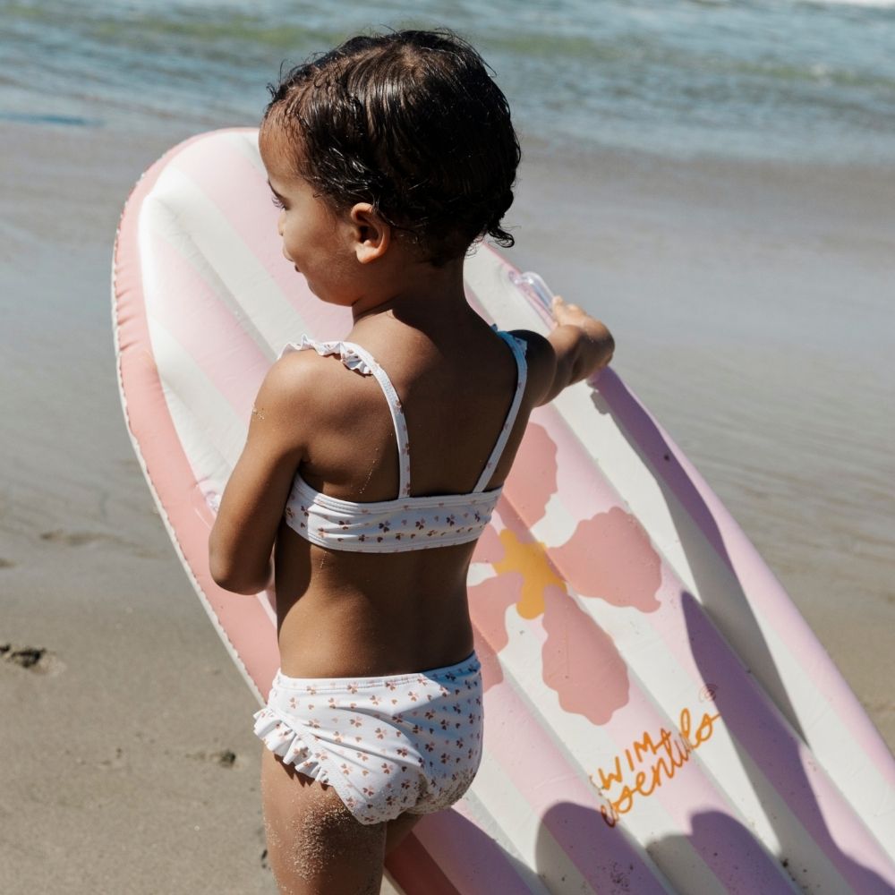 Kislány profilból a tengerparton a virágpiac mintás felfújható szörfdeszkával.