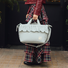 Divatos nő Walking Mum Matcha zöld kockás fodros pelenkázó táskával kávézó előtt